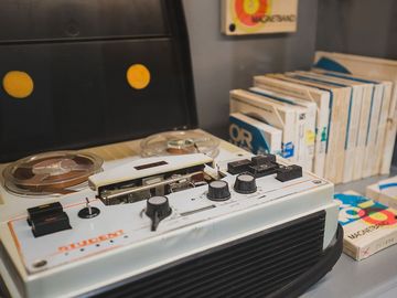 Das Bild zeigt ein Tonbandgerät und mehrere Tonbänder in Hüllen daneben.