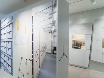 Das Bild zeigt eine Ausstellungswand, die einer Hebelschubanlage im Stasi-Unterlagen-Archiv nachempfunden wurde.