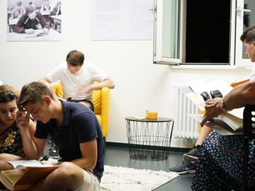 Menschen sitzen auf dem Boden und auf Stühlen und lesen in Stasi-Beispielakten.