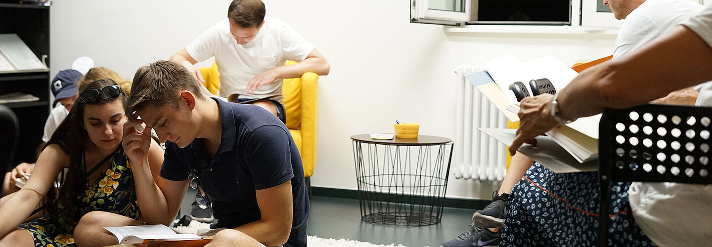 Menschen sitzen auf dem Boden und auf Stühlen und lesen in Stasi-Beispielakten.