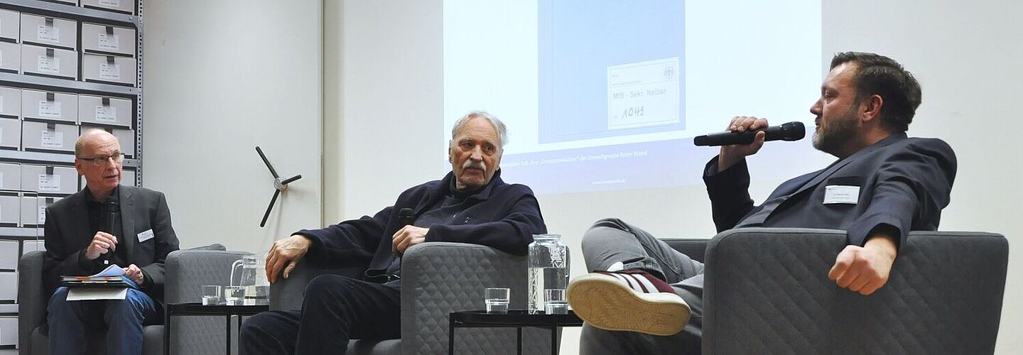 Drei Personen sitzen auf einer Bühne und sprechen miteinander.