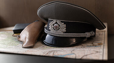 Das Foto zeigt eine Mütze, die zusammen mit einem Pistolenholster auf einer Karte liegt.