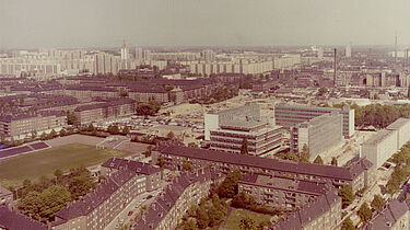 Farbige Luftaufnahme auf Häuser und einen Fußballplatz mit einer kleinen Tribüne.