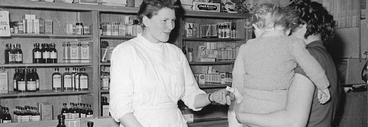 Frau mit Kind auf dem Arm spricht mit Apothekerin in Betriebsapotheke