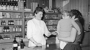 Frau mit Kind auf dem Arm spricht mit Apothekerin in Betriebsapotheke