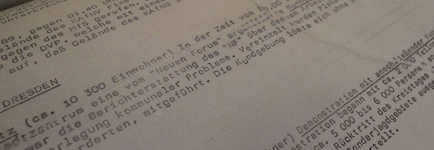 Blick in die Beispielakte Ein Blick in die aufgeschlagene Akte. Zu sehen sind mehrere Berichte aus verschiedenenen Städten der DDR. Die Seiten zeigen Spuren von Rissen.