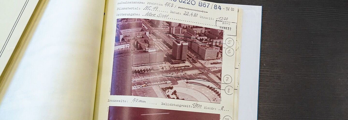 Ein Bild der aufgeschlagenen Beispielakte. Zu sehen sind zwei Fotos, die mit unterschiedlichem Zoom vom Fernsehturm aus aufgenommen wurden. Auf dem oberen Bild sieht man über den Alexanderplatz hinweg nach Nordosten. Im unteren Bild ist eine Reihe parkender Autos, die im oberen Bild zu erkennen war, in Nahaufnahme zu sehen.