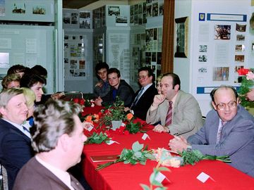 Auf dem Bild sieht man Stasi-Mitarbeiter an einer Festtafel. Im Hintergrund sind die Ausstellungstafeln des Traditionskabinetts zu sehen.