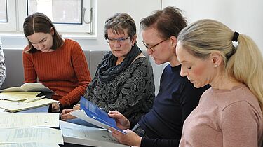 Auf dem Bild sieht man vier Personen an einem Tisch, die in Beispielakten und zusätzlichem Material lesen.
