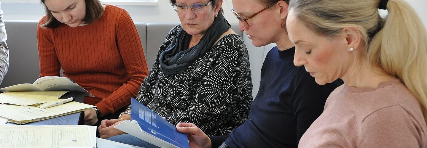 Auf dem Bild sieht man vier Personen an einem Tisch, die in Beispielakten und zusätzlichem Material lesen.