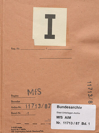Bild eines Aktendeckels. Er ist orange, mittig ist eine große römische eins aufgeklebt. Unten steht mehrfach die Archivsignatur „AIM Nr. 11713/87' und der Stempel „MfS“. Dieselben Informationen finden sich noch einmal auf einem Aufkleber des Bundesarchivs.