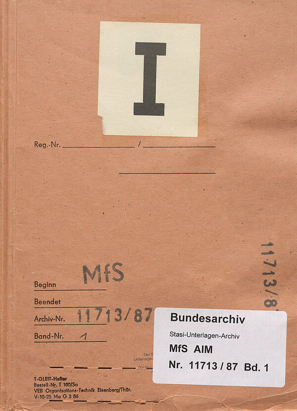 Bild eines Aktendeckels. Er ist orange, mittig ist eine große römische eins aufgeklebt. Unten steht mehrfach die Archivsignatur „AIM Nr. 11713/87" und der Stempel „MfS“. Dieselben Informationen finden sich noch einmal auf einem Aufkleber des Bundesarchivs.