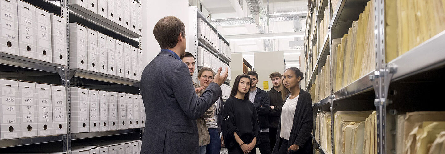 A group of teenagers is listening to a tour guide amongst the shelves of files.