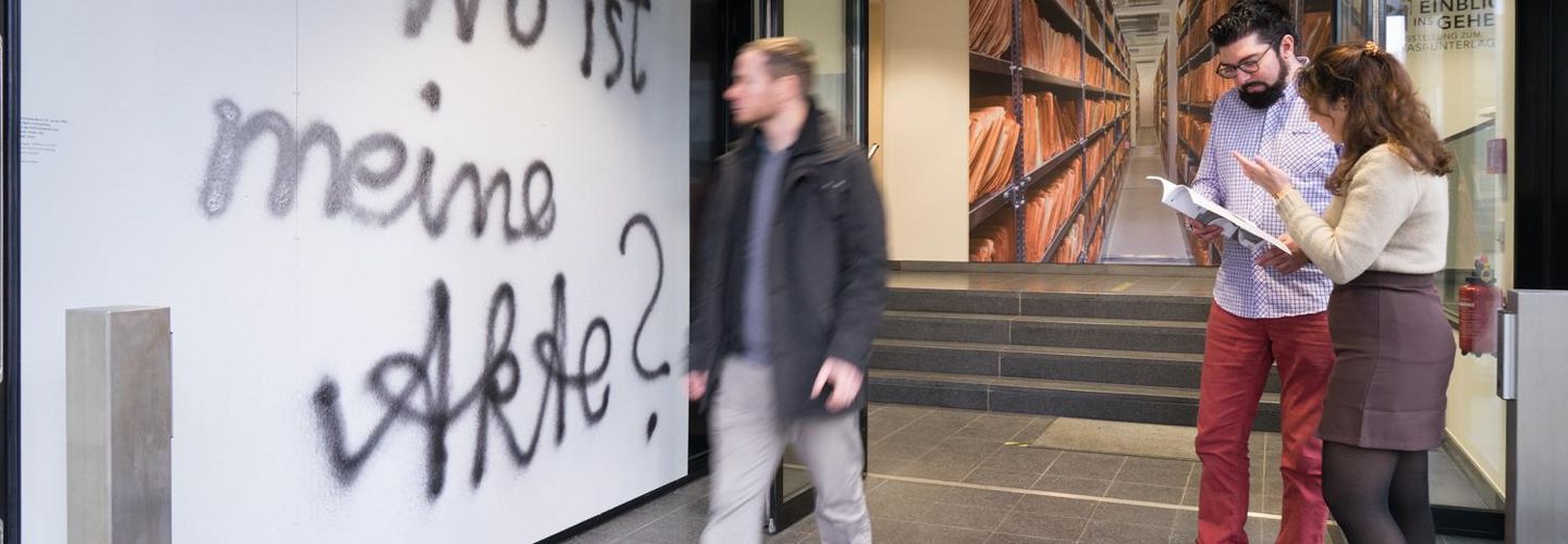 Das Bild zeigt Besuchende im Eingangsbereich der Ausstellung 'Einblick ins Geheime'. An einer Wand steht: 'Wo ist meine Akte?'