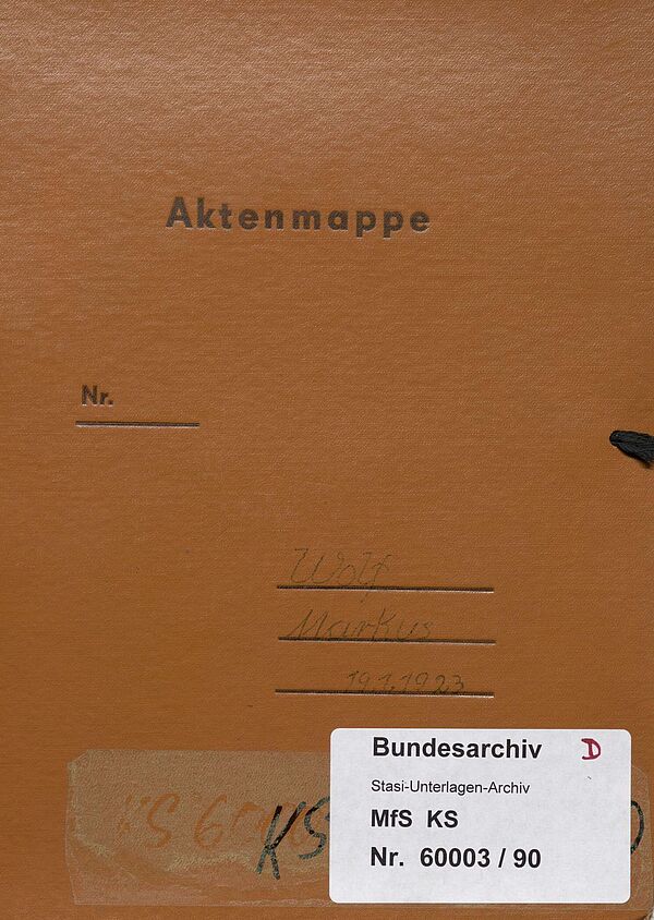 Ein rotbrauner Aktendeckel. Oben steht aufgedruckt "Aktenmappe". Der Name Markus Wolf ist auf einige Linie geschrieben. Unten ist ein Aufkleber des Bundesarchivs mit der Aktensignatur MfS, KS, Nr. 60003/90.