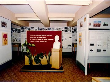 Auf dem Bild ist die Ausstellung der Hauptabteilung XX der Stasi zu sehen. In der Mitte eine Büste von Felix Dzierżyński vor einer Wand mit einem Titat. Rundherum sieht man Ausstellungstafeln.